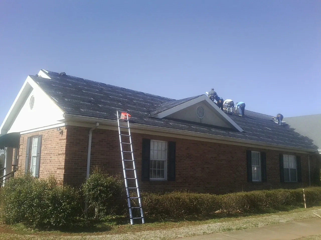 Crew tearing shingles off a brick ranch roof with a ladder set — Emergency Roof Repair work by our crew in Diagonal