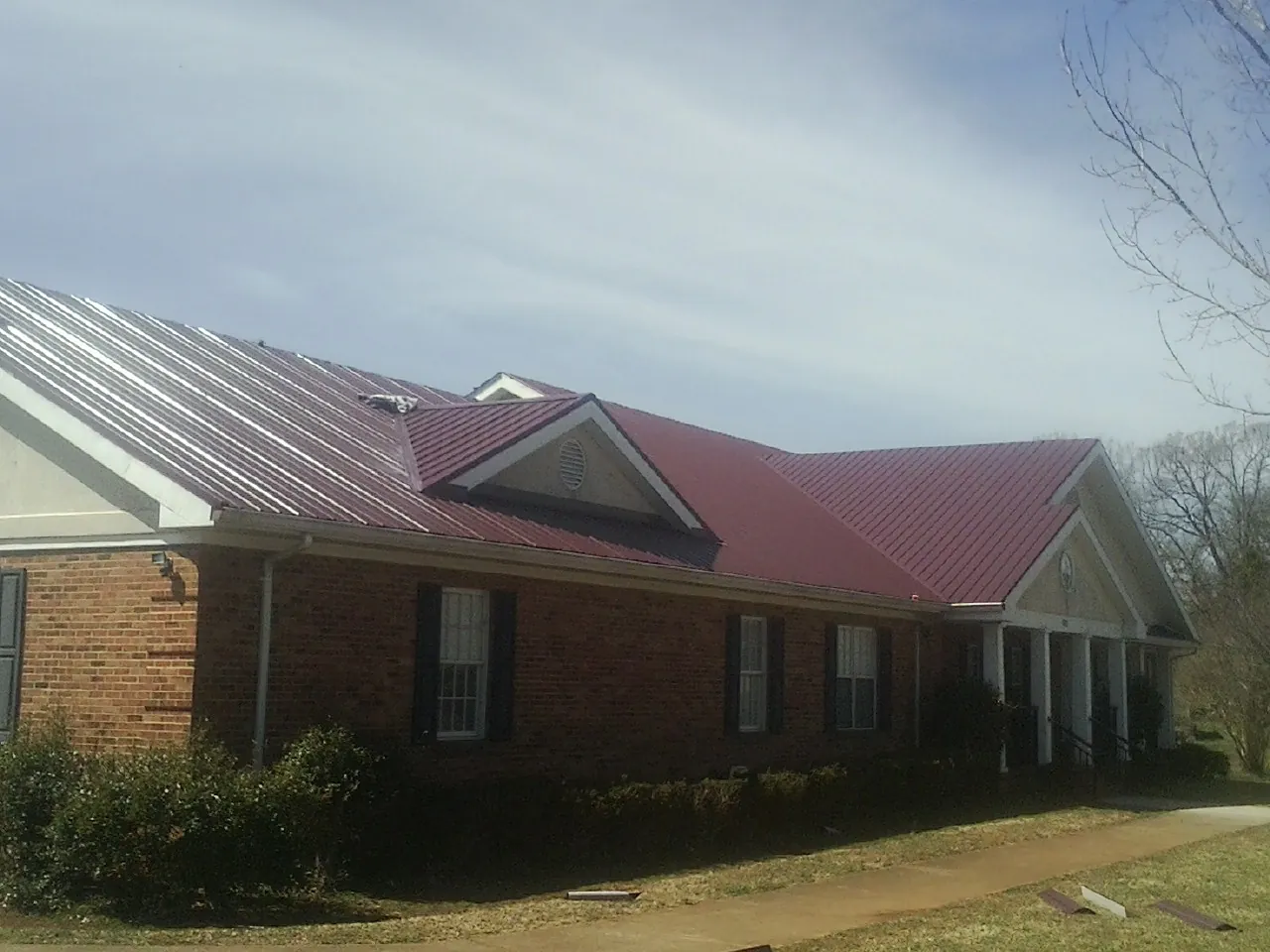 Red metal roof with gabled entries on a long brick building, from a Hail Damage Roof Repair job in Diagonal