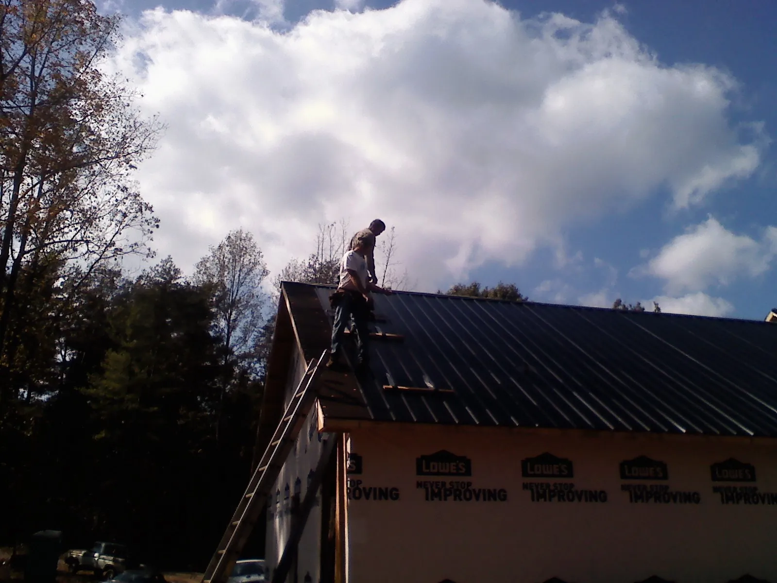 Roofer fastening dark metal panels high against a cloudy sky, from a Roof Inspection job in Diagonal