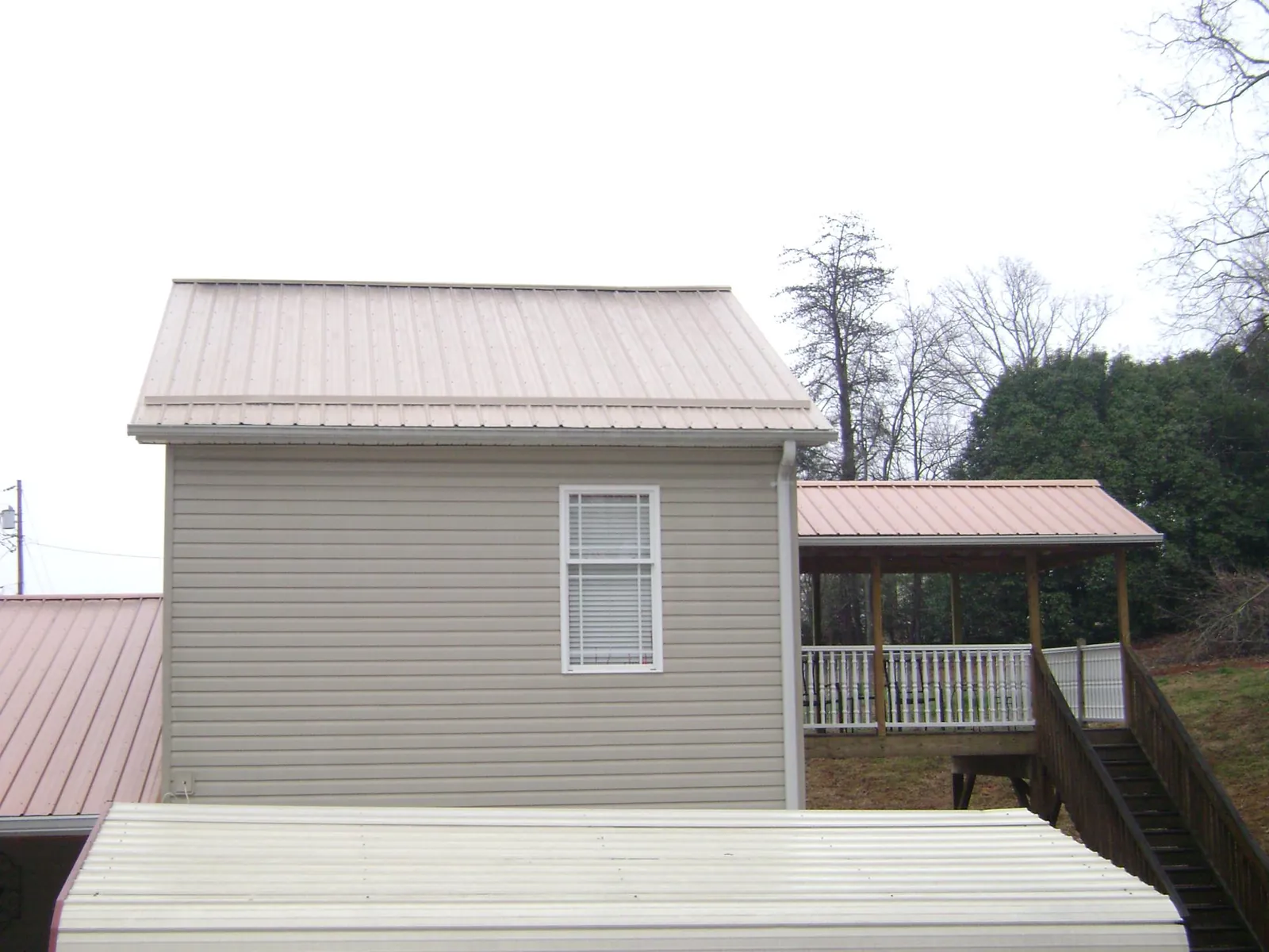Tan metal roofs on a two story addition and attached porch, from a Roof Replacement job in Diagonal